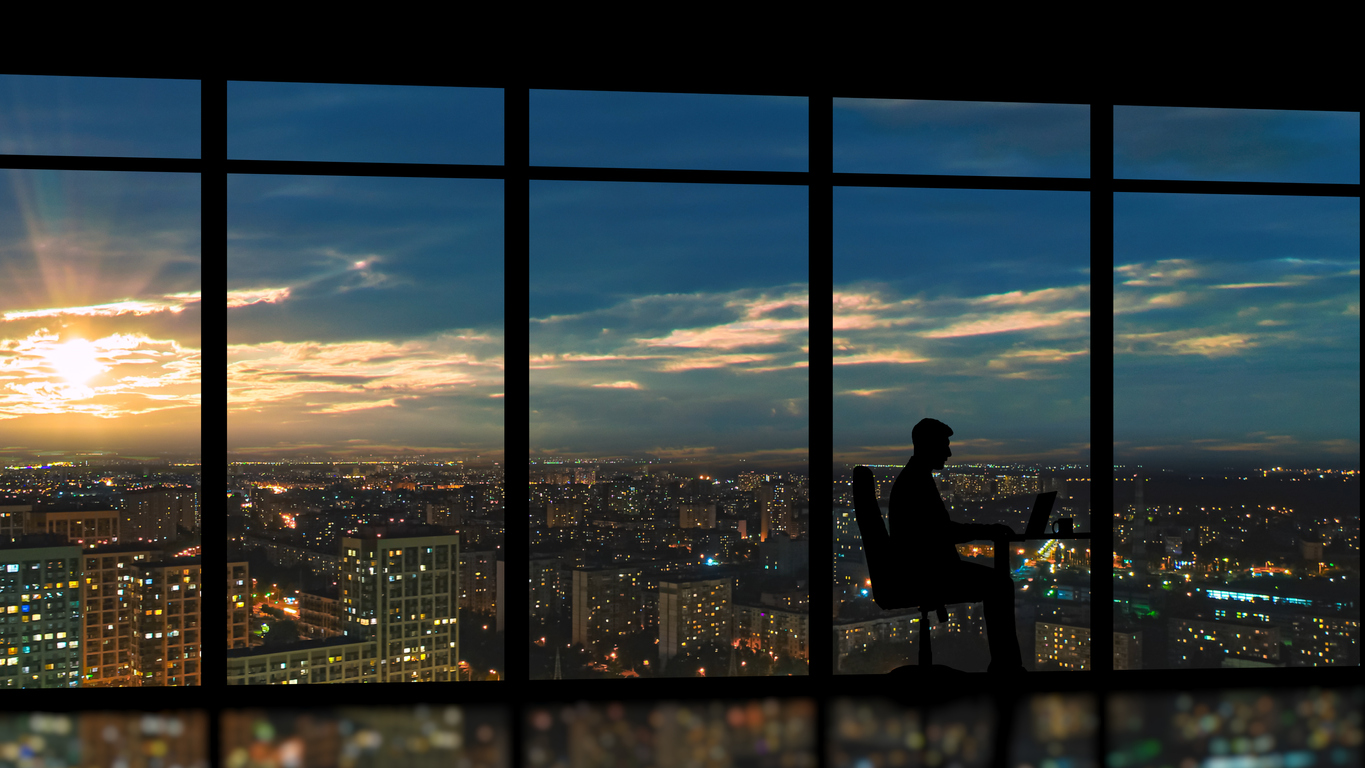The businessman sitting near the panoramic window against the city sunrise The businessman sitting near the panoramic window against the city sunrise