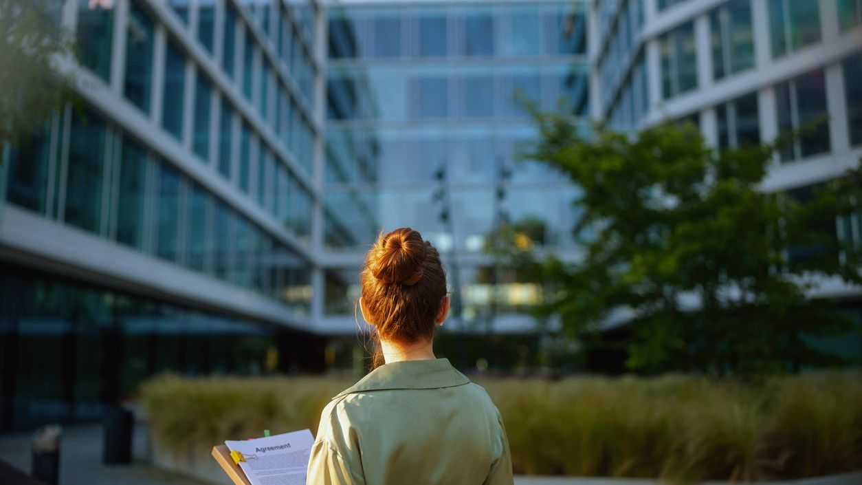 Seen from behind business woman near office building Seen from behind business woman near office building in green blouse with documents.